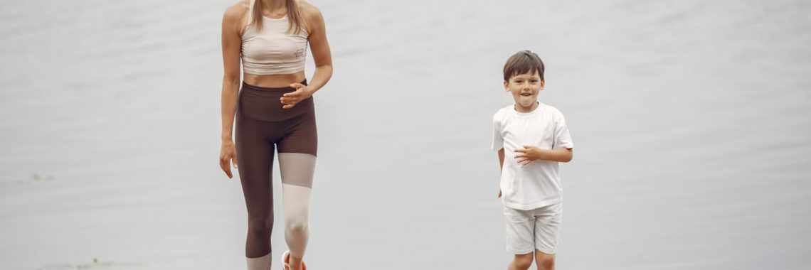 A woman and young boy jogging together on a wooden pier by a tranquil lake, enjoying leisure time outdoors.